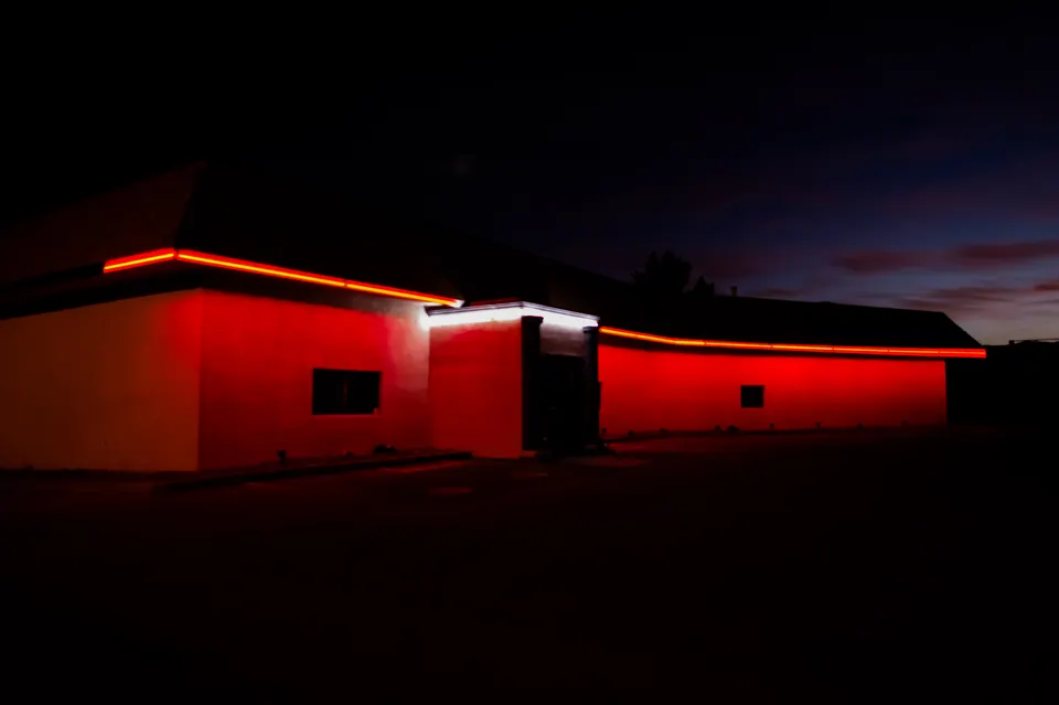 A red strip of neon traces the roof of a low building beneath a dark sky.
