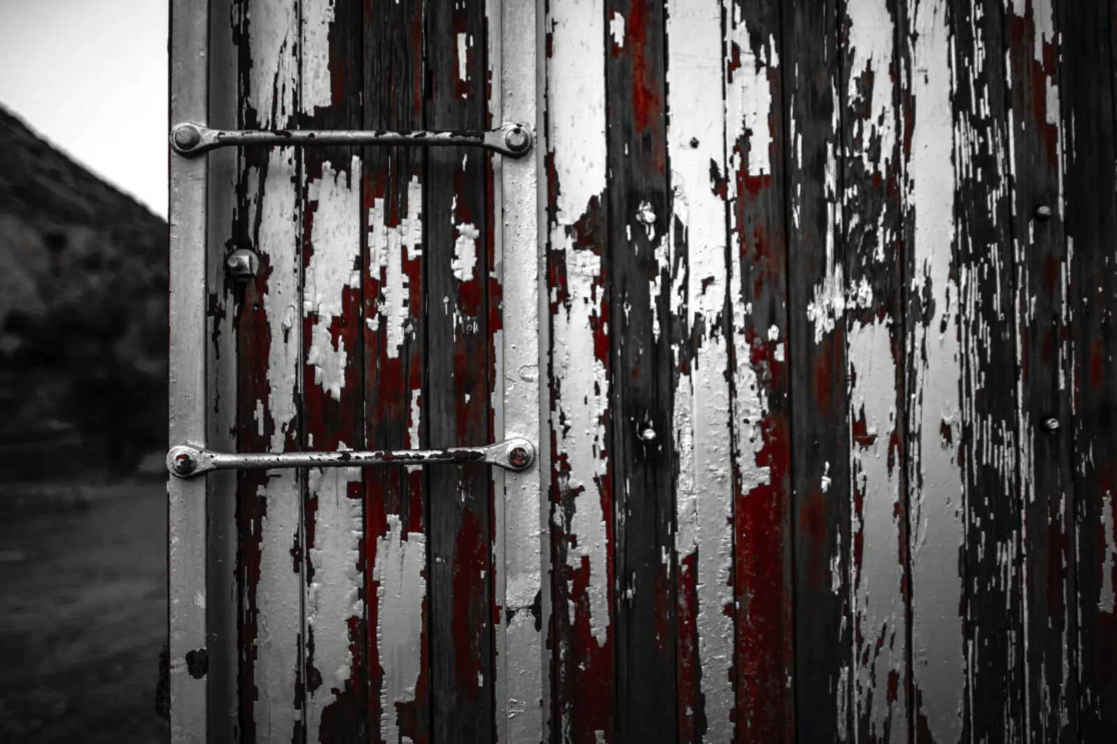 Peeling white paint exposes strips of red on old wooden doors.