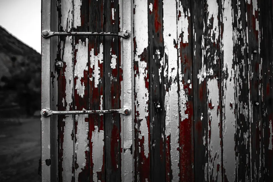 Peeling white paint exposes strips of red on old wooden doors.