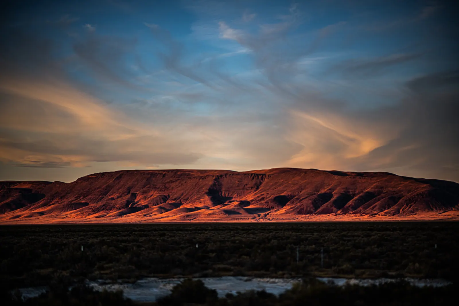 Low red hills sit below sweeping blue and gold evening clouds.