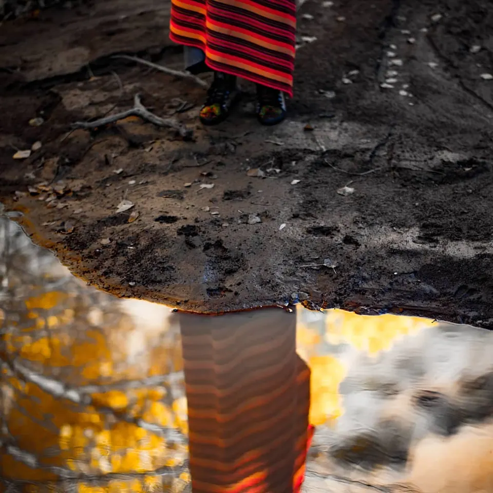 A striped red object is reflected in a small puddle beside dark ground.