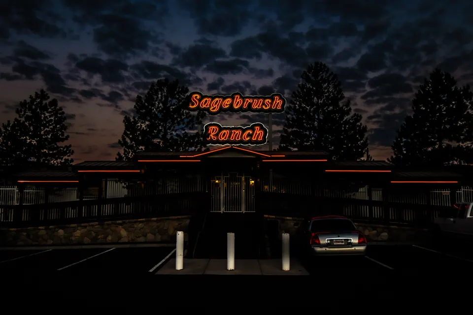 A glowing roadside sign appears above a dark building beneath a textured evening sky.