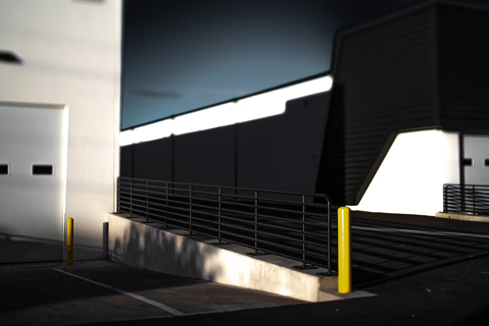 Sharp sunlight and shadow divide a pale building and an outdoor staircase.