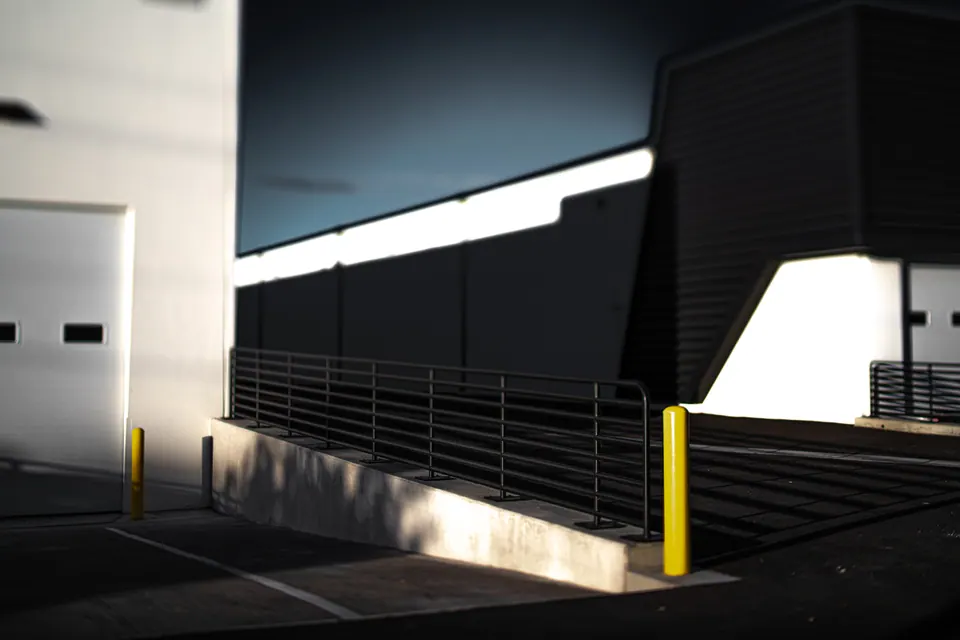 Sharp sunlight and shadow divide a pale building and an outdoor staircase.