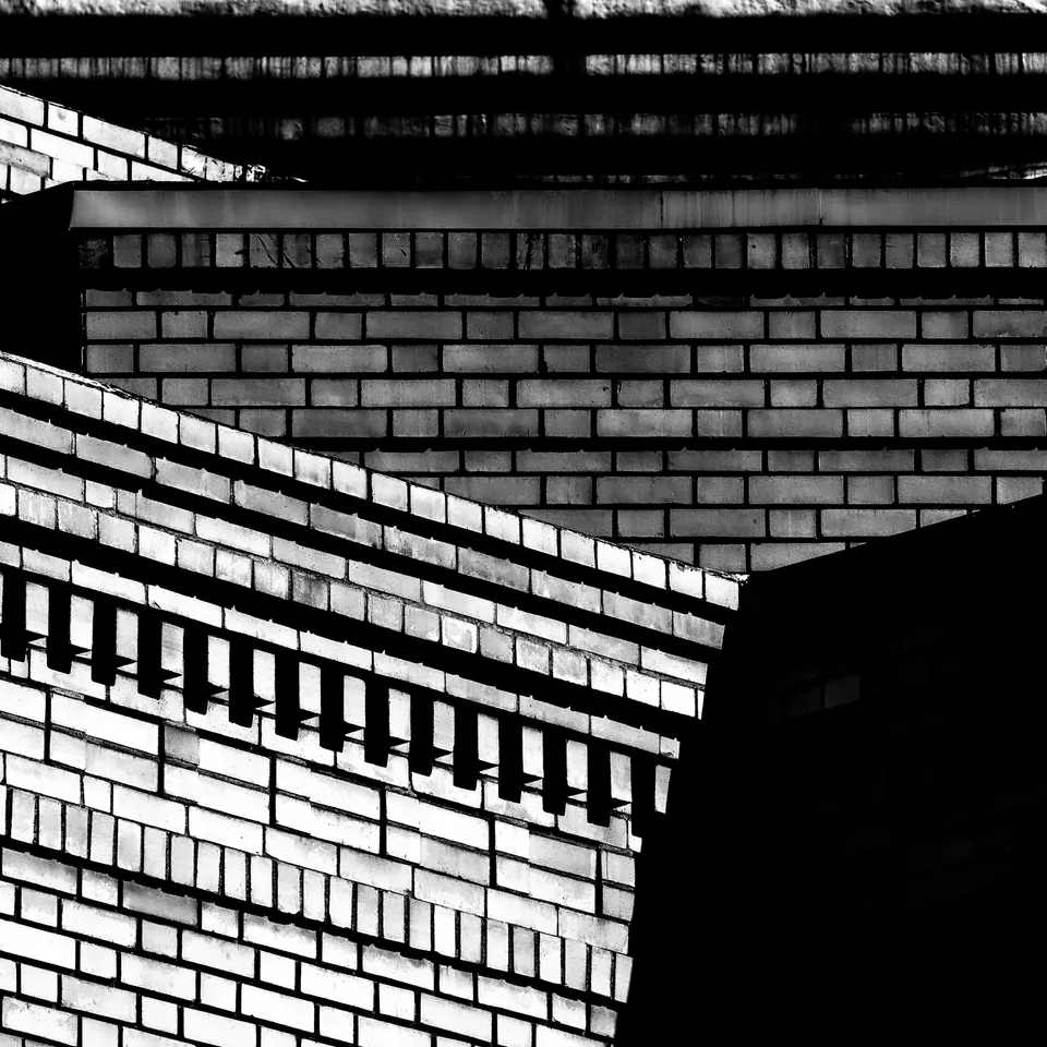 Dark railings cast sharp lines across a bright brick wall.