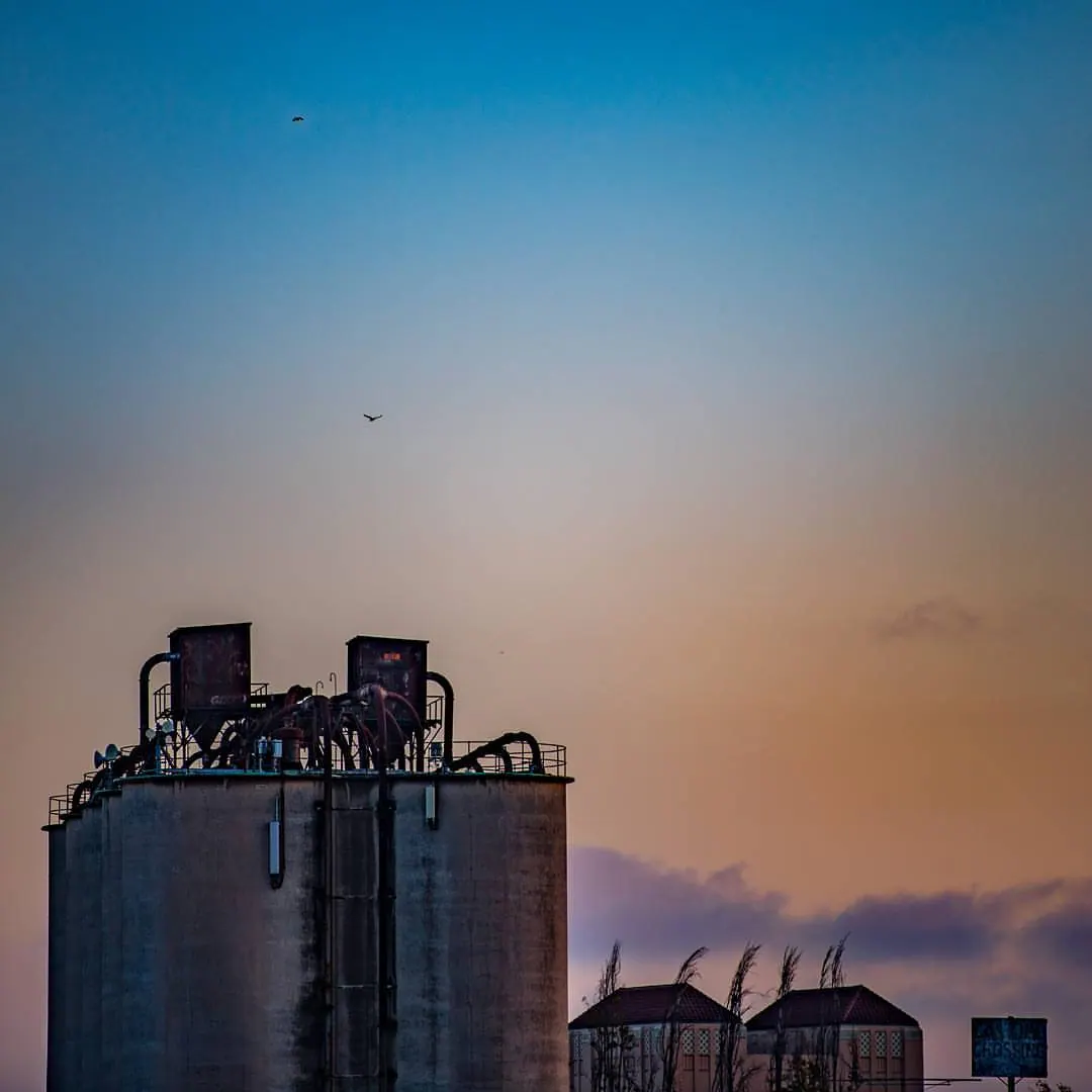 Tall industrial silos rise beneath a pale evening sky and a soft cloud of steam.