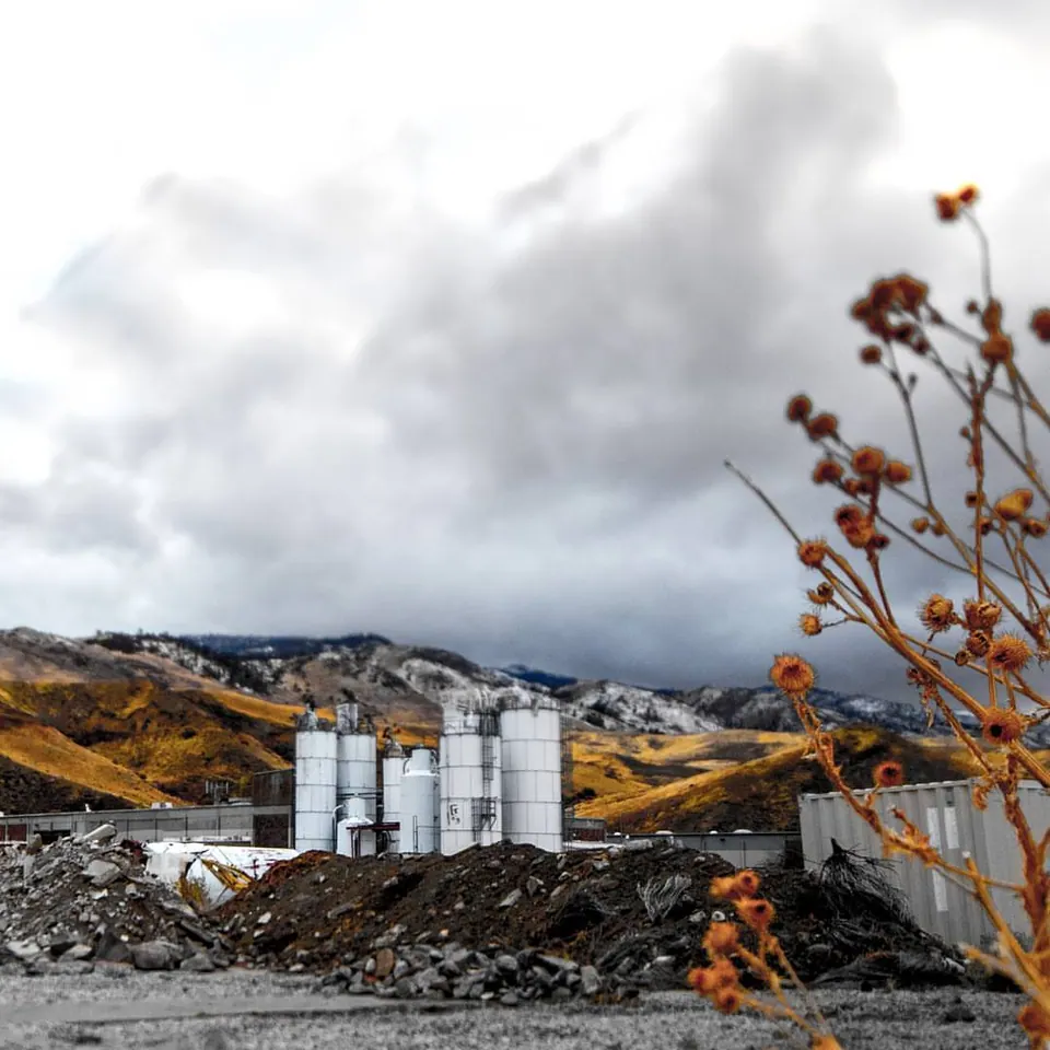 Pale industrial silos sit beneath a low, cloud-covered hillside.
