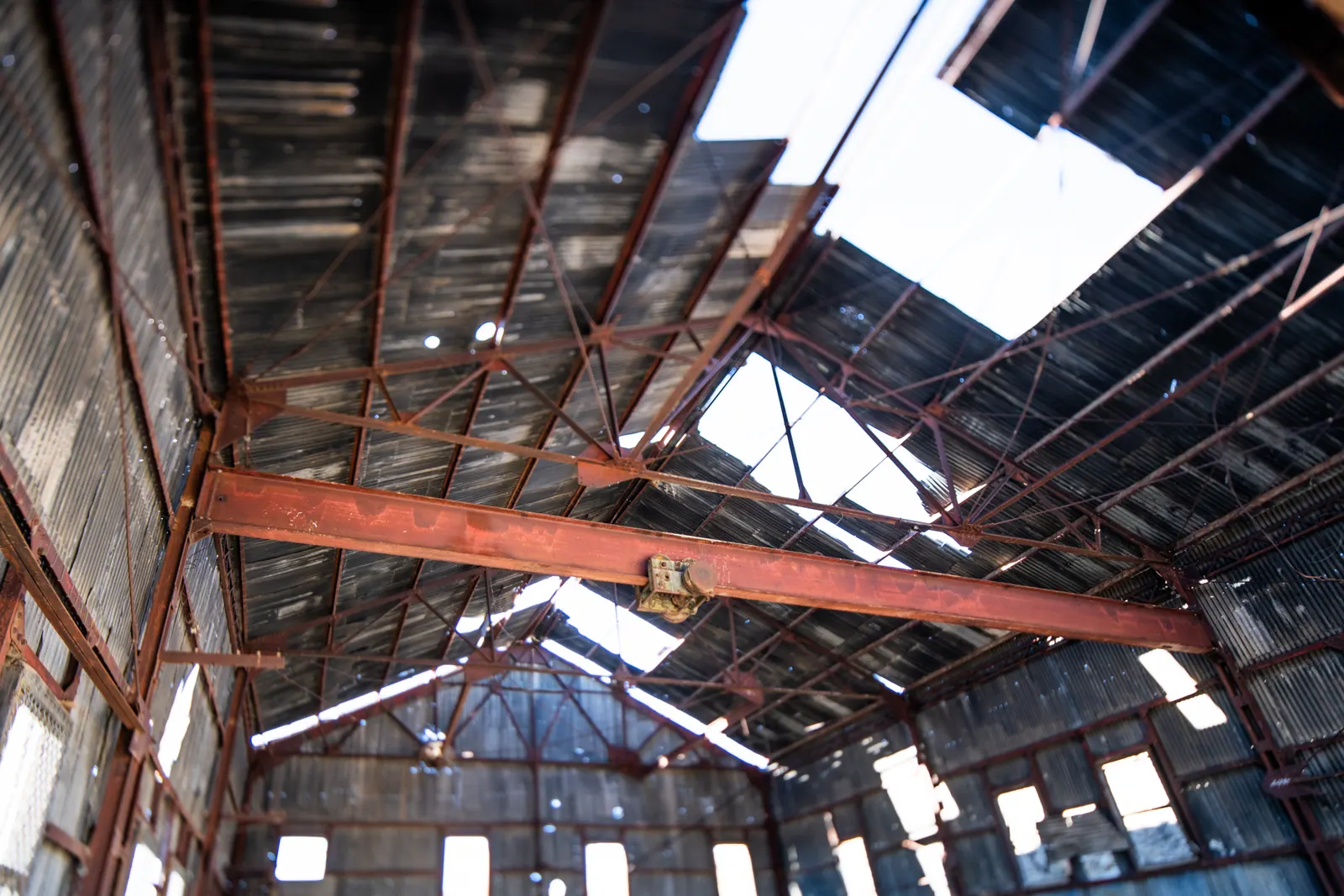 Broken roof panels expose bright sky above the timber frame of an old building.
