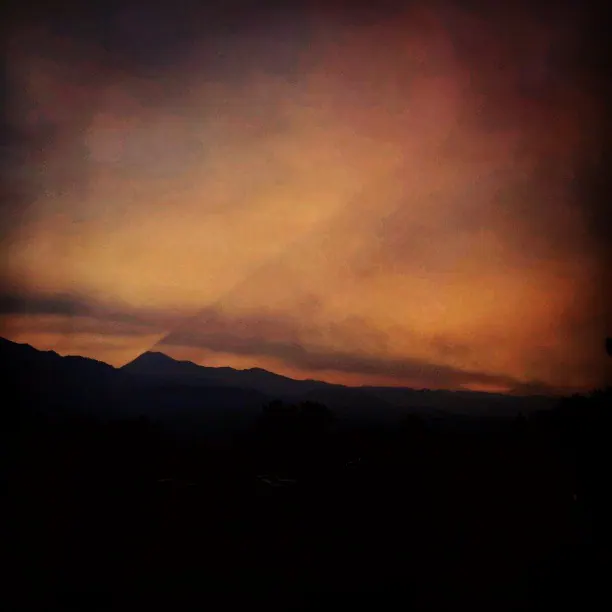 An orange cloud or plume of smoke spreads above a dark mountain ridge.