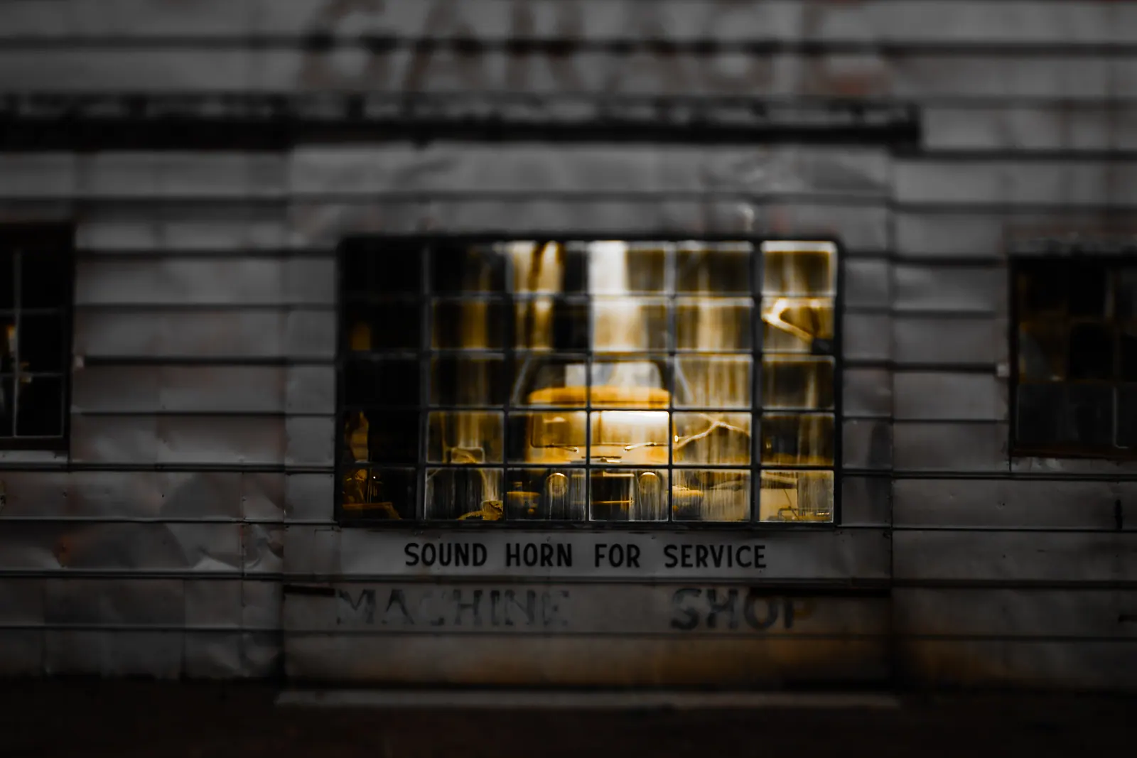 A small window and faded lettering punctuate the wall of an old workshop.