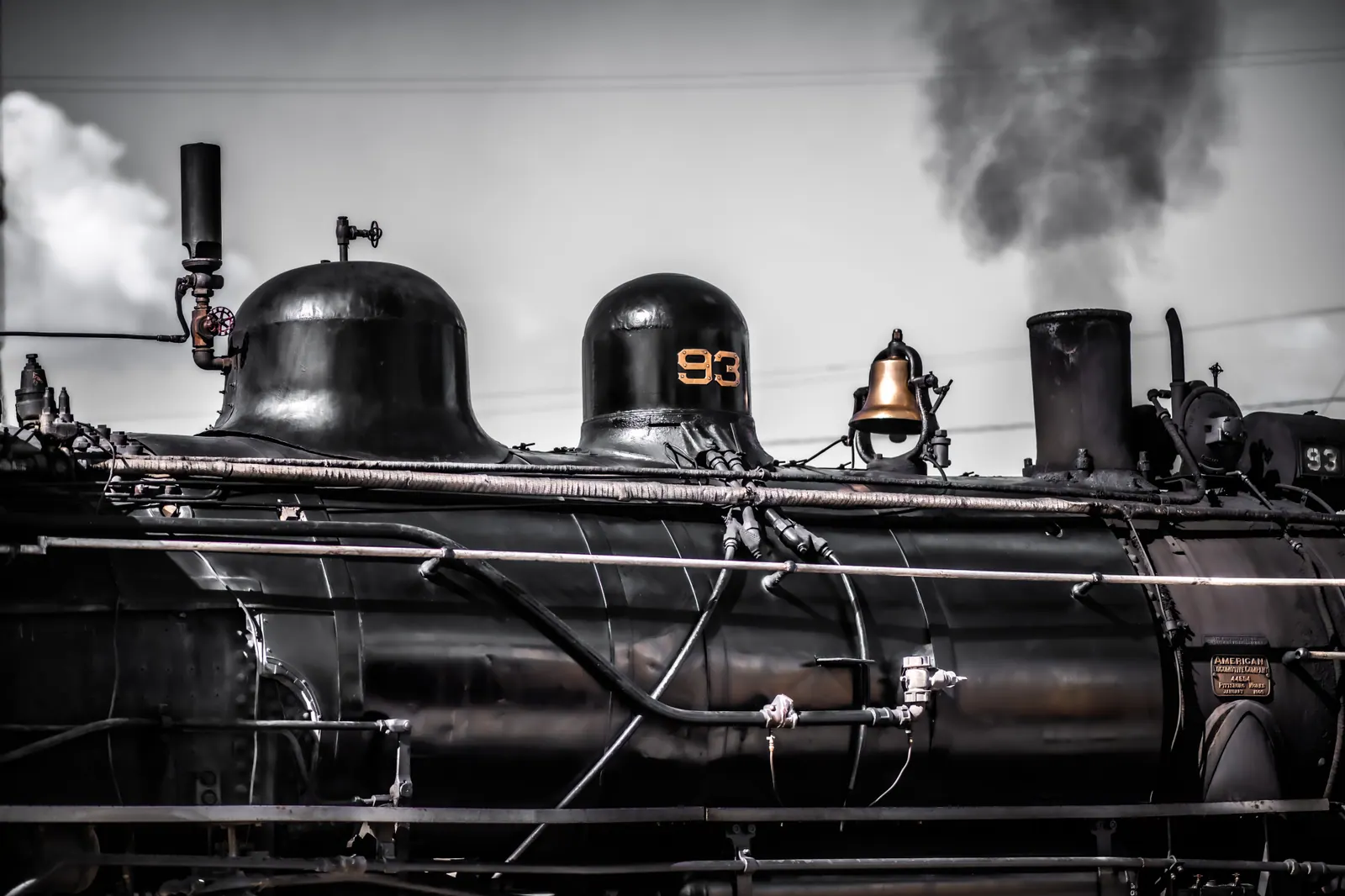 Steam billows behind the dark wheels and pipework of a vintage locomotive.
