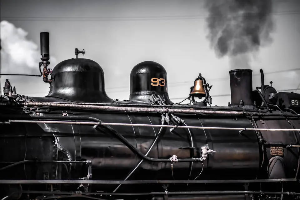 Steam billows behind the dark wheels and pipework of a vintage locomotive.