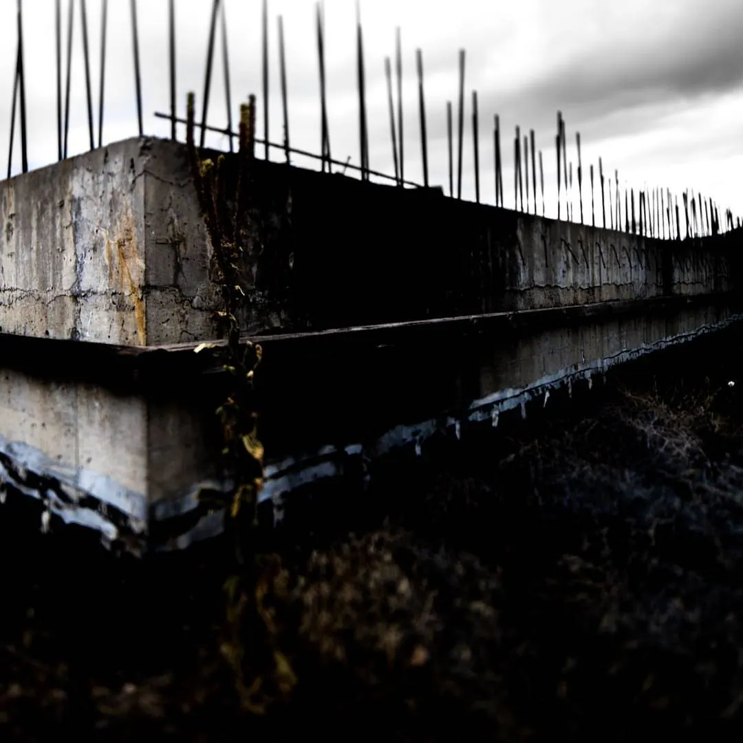 Rows of thin steel rods project from the edge of a rough concrete structure.