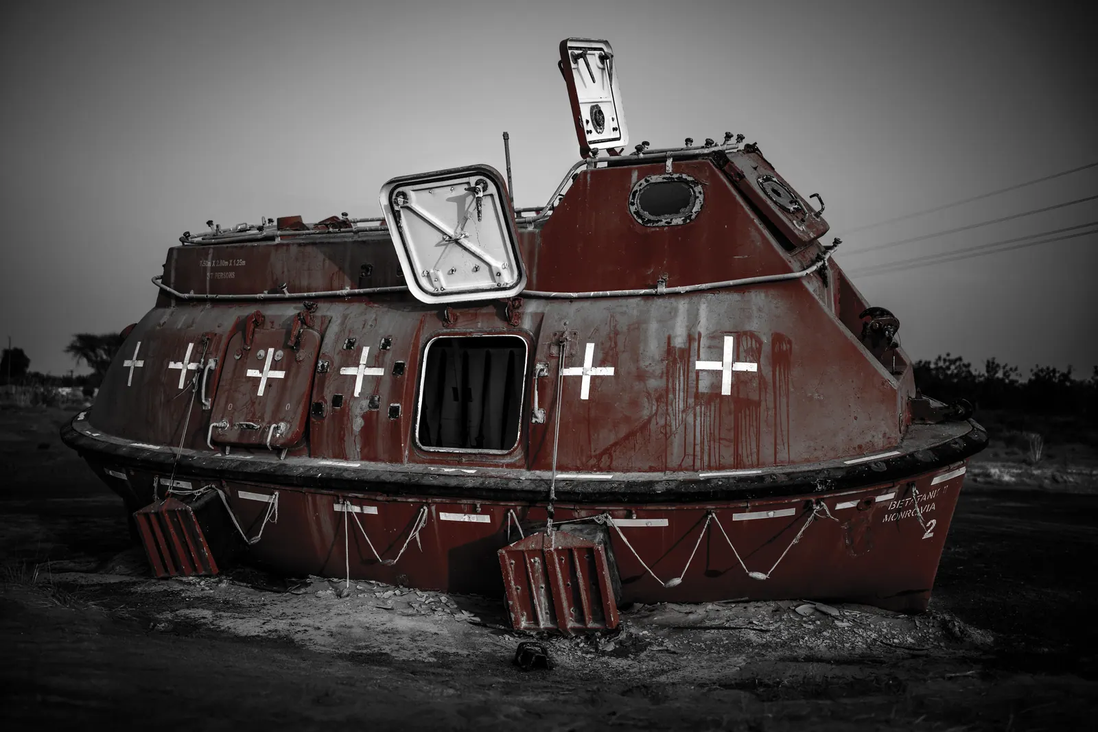 A weathered red wooden boat rests on land beneath a grey sky.