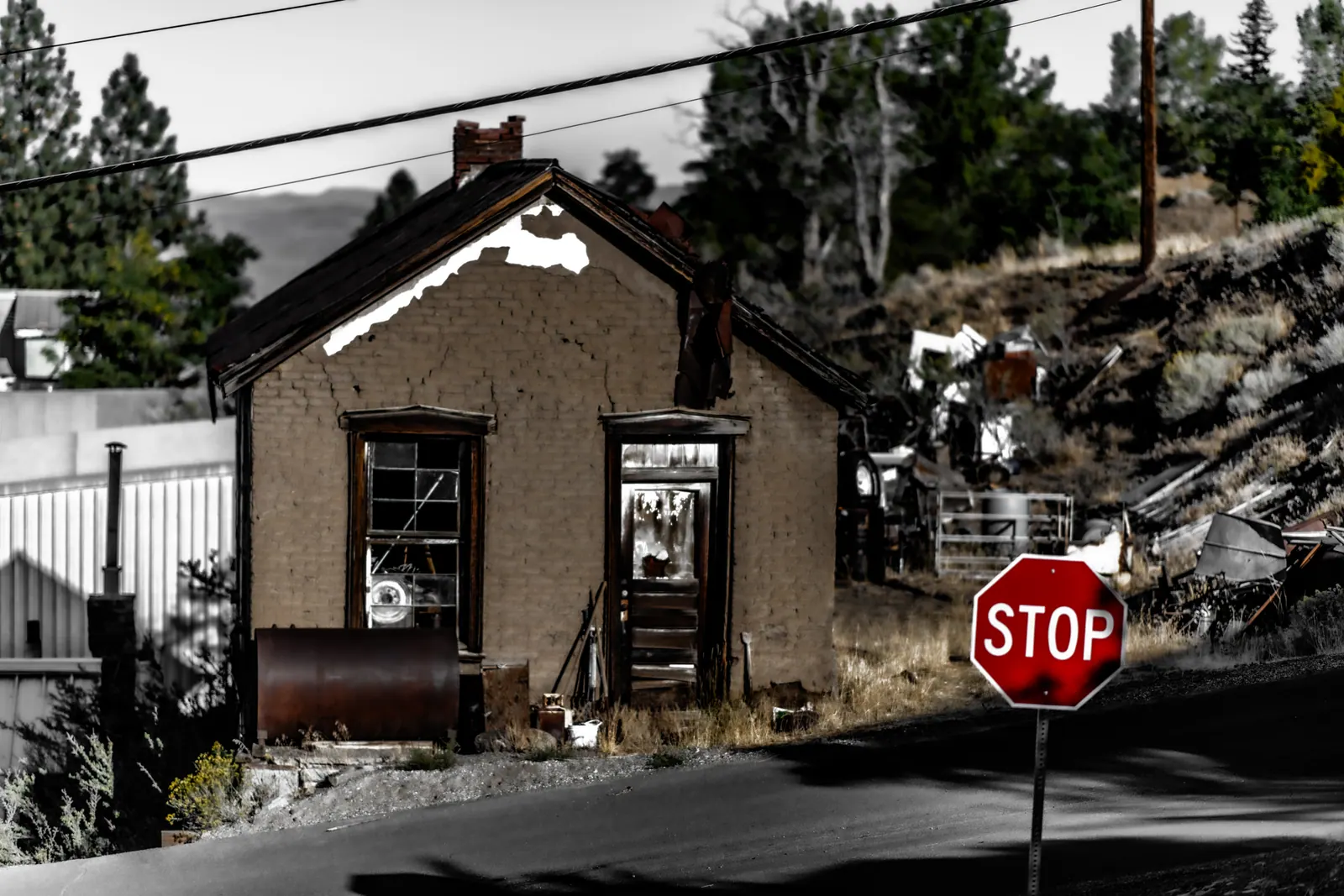 A red stop sign stands beside a small stone building on a quiet street.