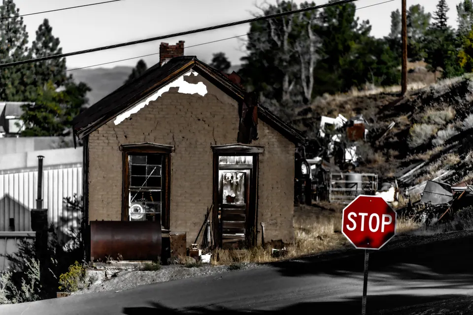 A red stop sign stands beside a small stone building on a quiet street.