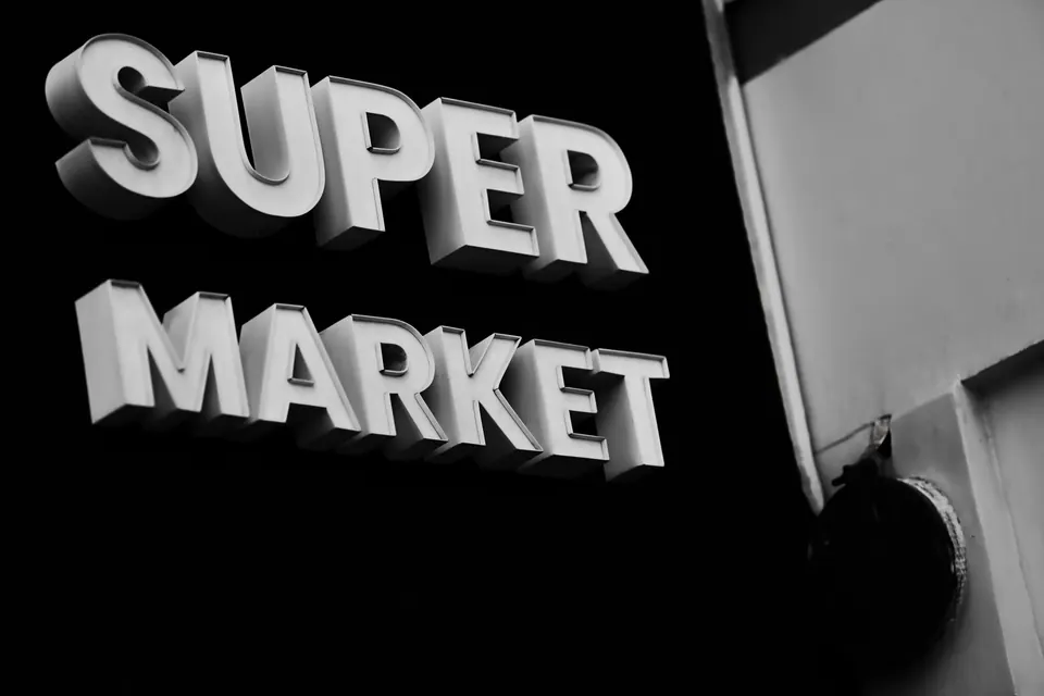 White supermarket lettering projects from a dark building facade in black and white.