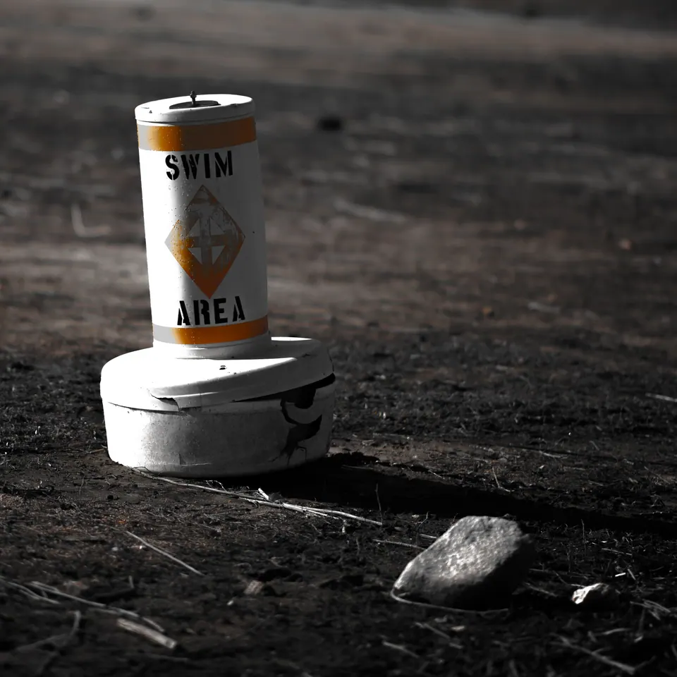 A small can marked Swim Area stands on a round base against dark ground.