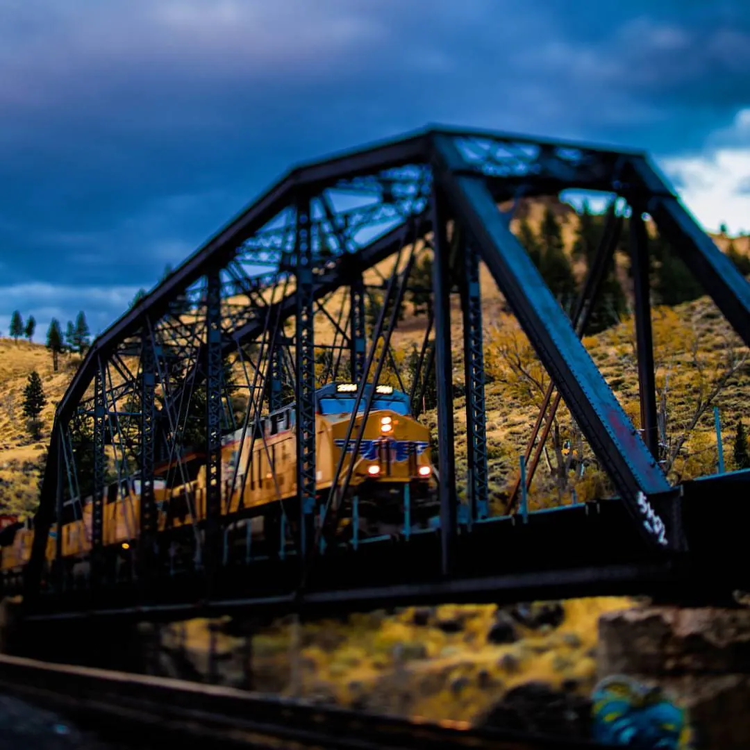 A blue metal truss bridge spans a river beneath a softly coloured sky.