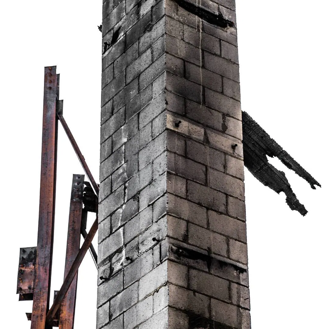 A tall brick chimney and a dark beam remain against a pale sky.