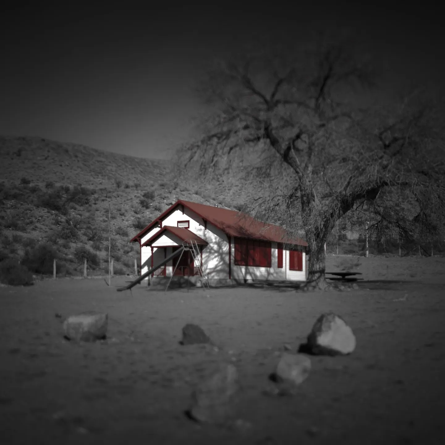 A red and white cabin stands beside a bare tree in a pale, snowy landscape.