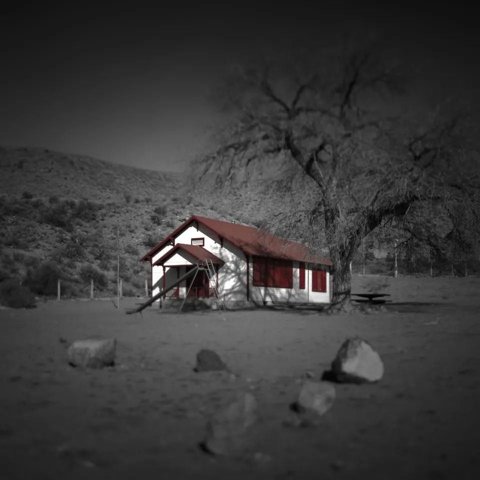 A red and white cabin stands beside a bare tree in a pale, snowy landscape.