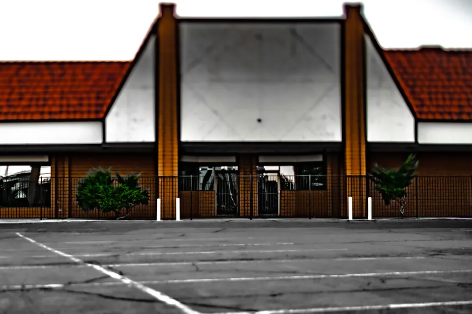 A symmetrical building with a red roof faces an empty marked parking area.