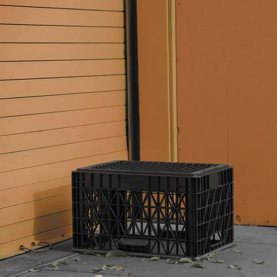 A dark plastic crate rests against a warm yellow exterior wall.