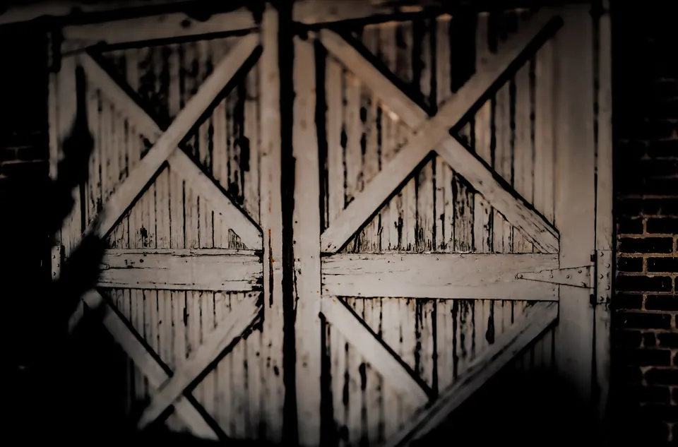 Two large wooden doors show diagonal bracing, peeling paint and dark hinges.