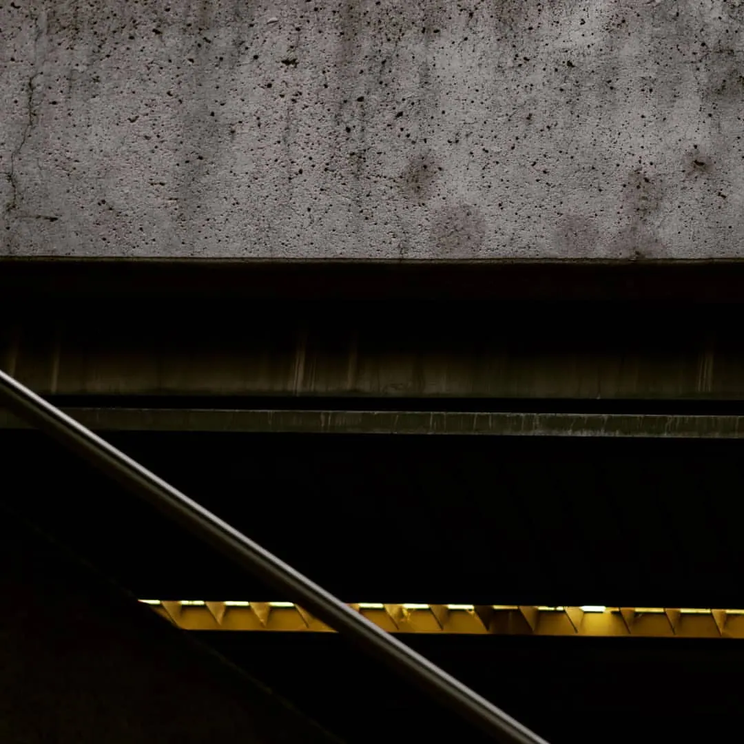Dark rails and a yellow line form a strong diagonal beneath a concrete wall.