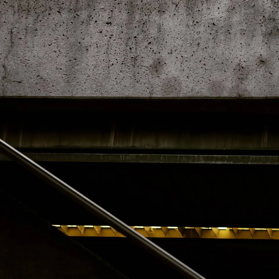 Dark rails and a yellow line form a strong diagonal beneath a concrete wall.