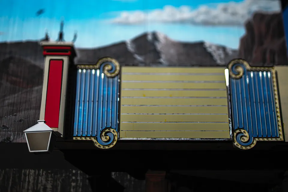 A blank signboard with colourful trim stands against a softly blurred streetscape.