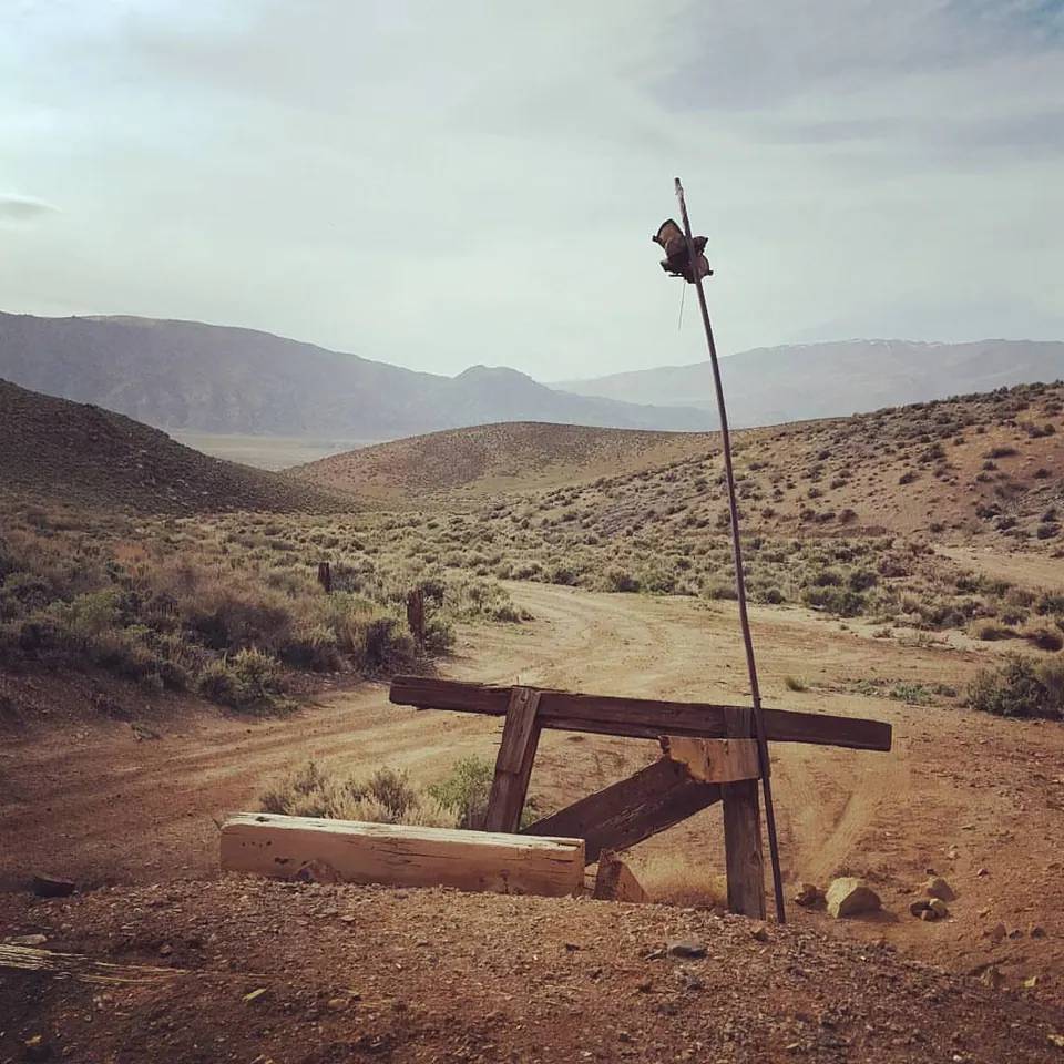 An empty picnic table rests in a dry desert clearing below distant hills.
