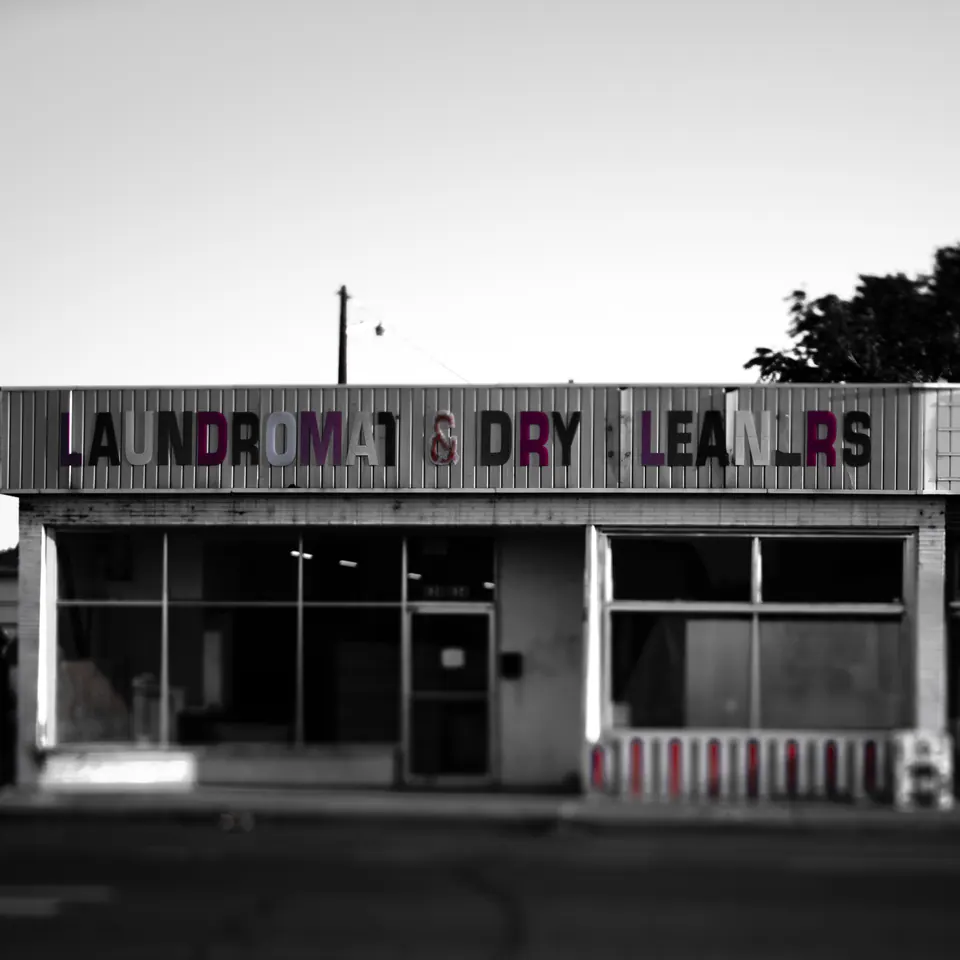 Faded laundry and dry-cleaning lettering runs above a row of dark windows.