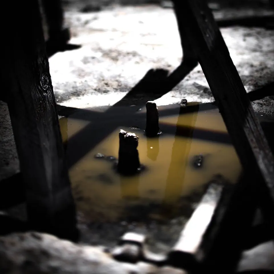 Dark beams frame standing water and small objects inside an abandoned structure.