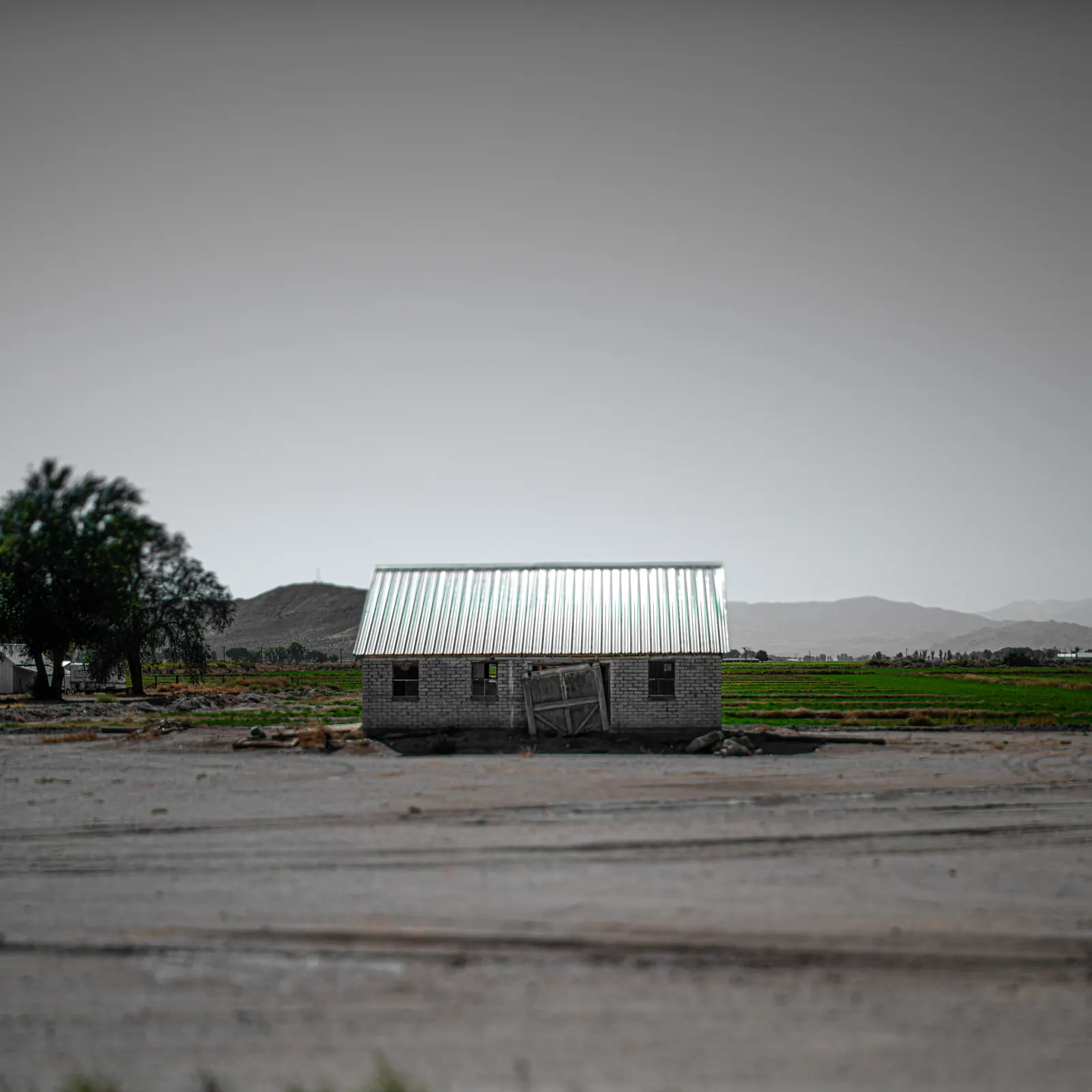 A small building with a pale green roof sits beside an empty road.
