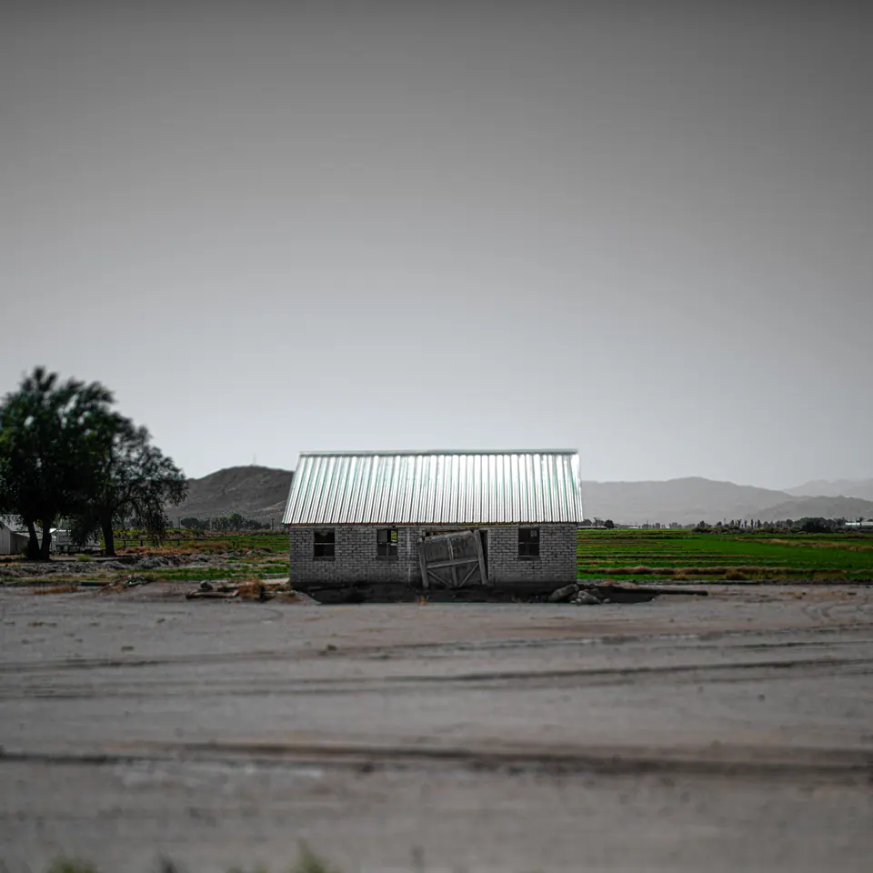 A small building with a pale green roof sits beside an empty road.