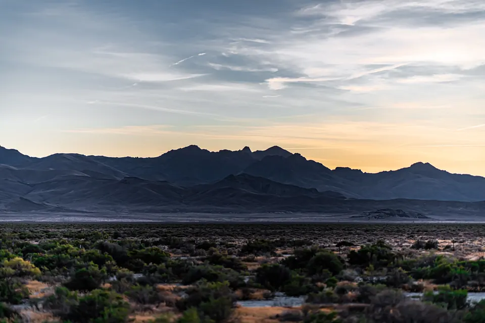 A soft strip of evening colour sits above dark mountains and desert plants.