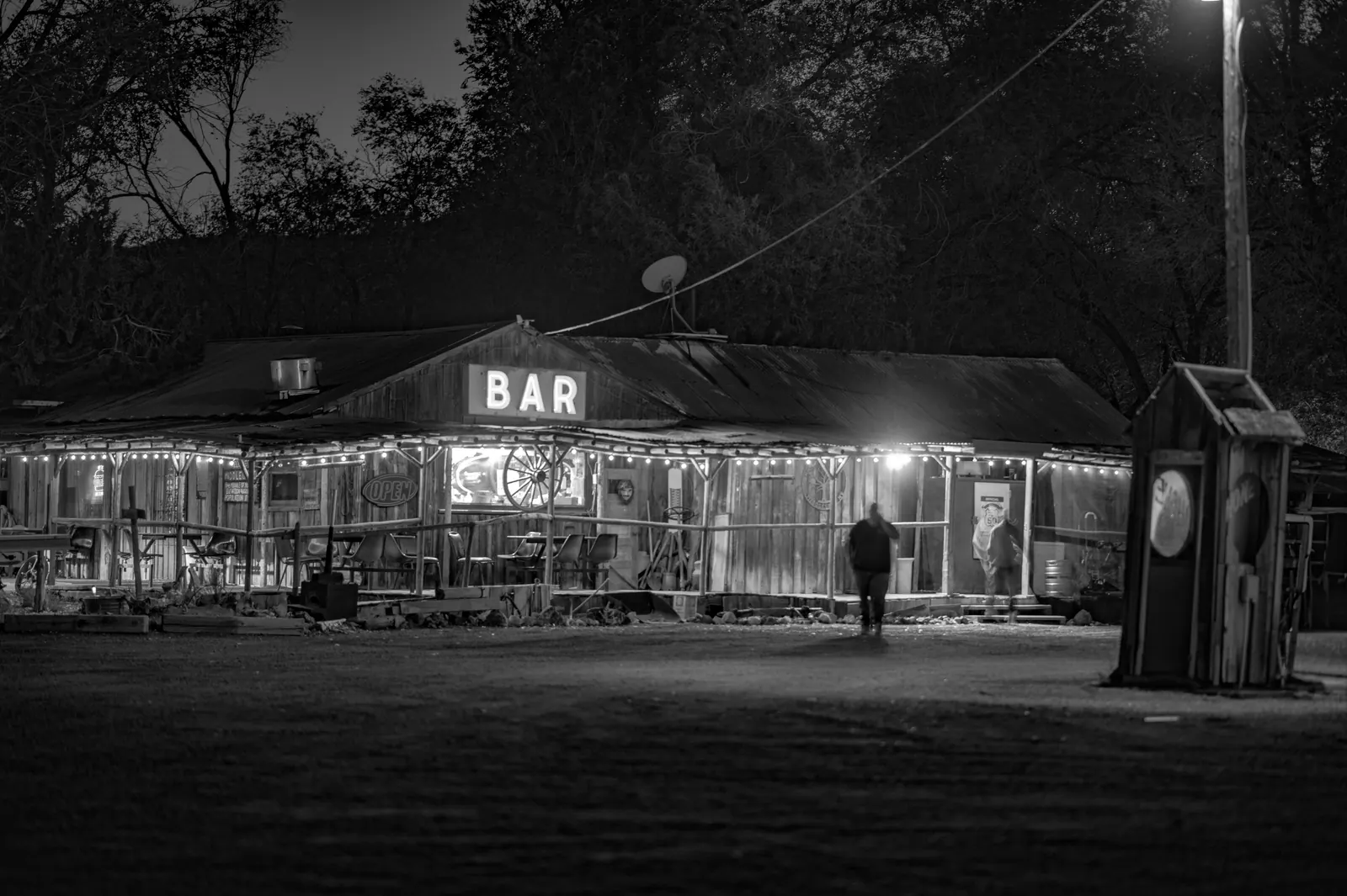A small roadside bar glows at night, its sign bright against the surrounding dark.