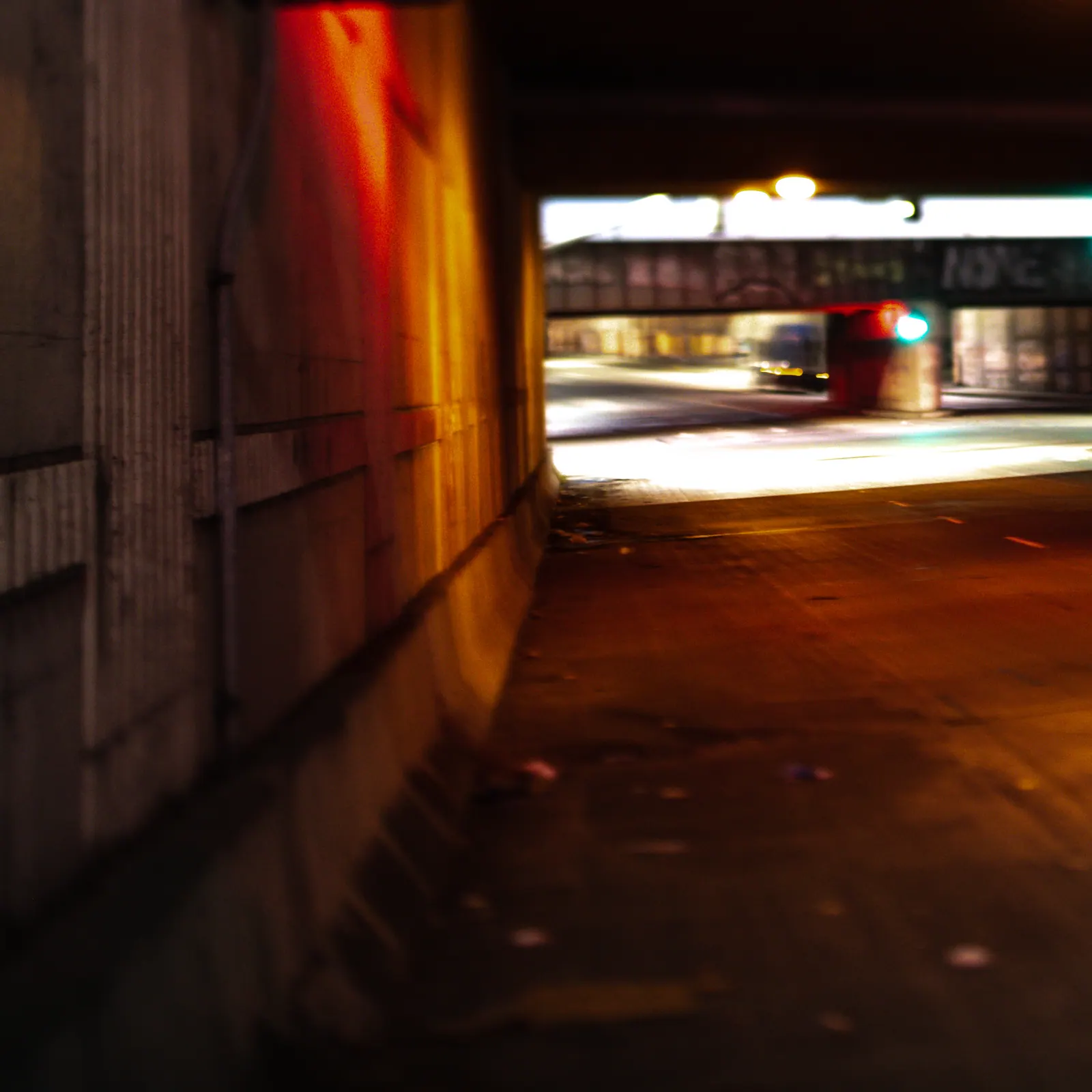 Warm light runs along a narrow passage toward a blurred street at night.