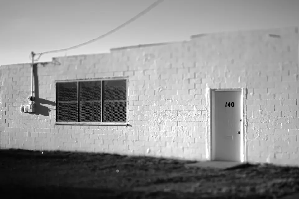 A small window and narrow door punctuate the front of a low white building.