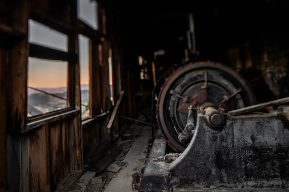 A large metal wheel sits in the dusty interior of an old wooden building.