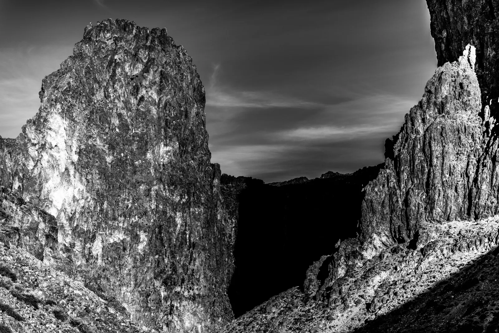 Tall, rough rock walls frame a dark canyon in black and white.