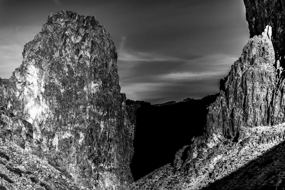 Tall, rough rock walls frame a dark canyon in black and white.