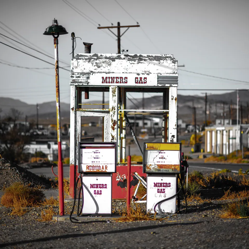A weathered fuel pump stands beneath wires and a pale sky.