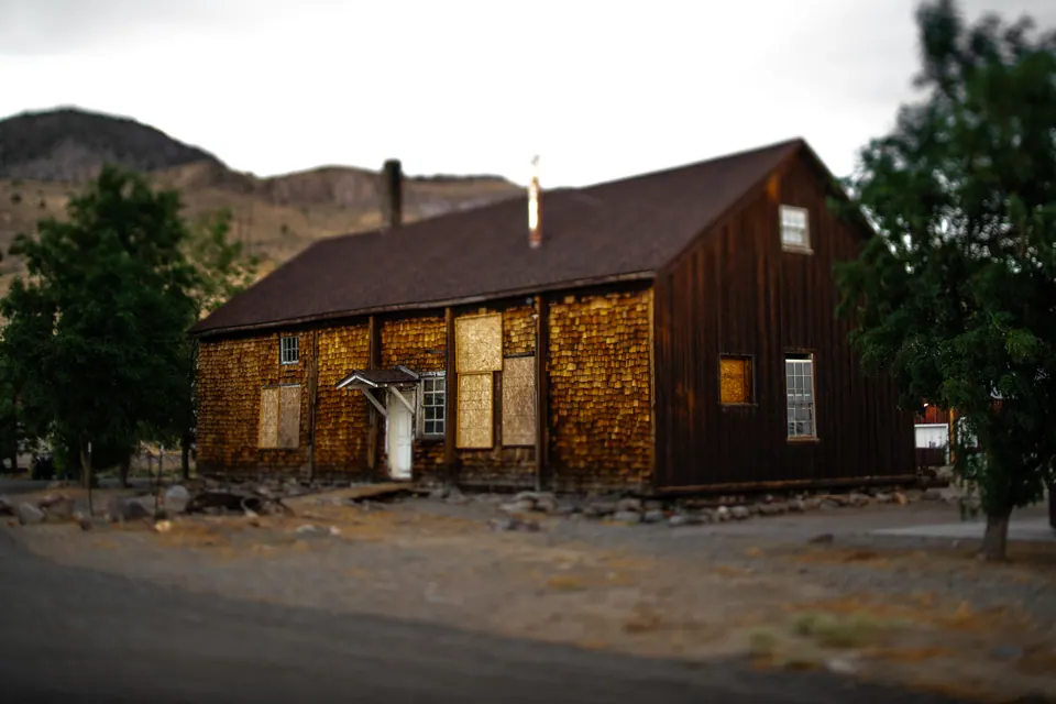A brown wooden building stands beside a quiet street beneath leafy trees.