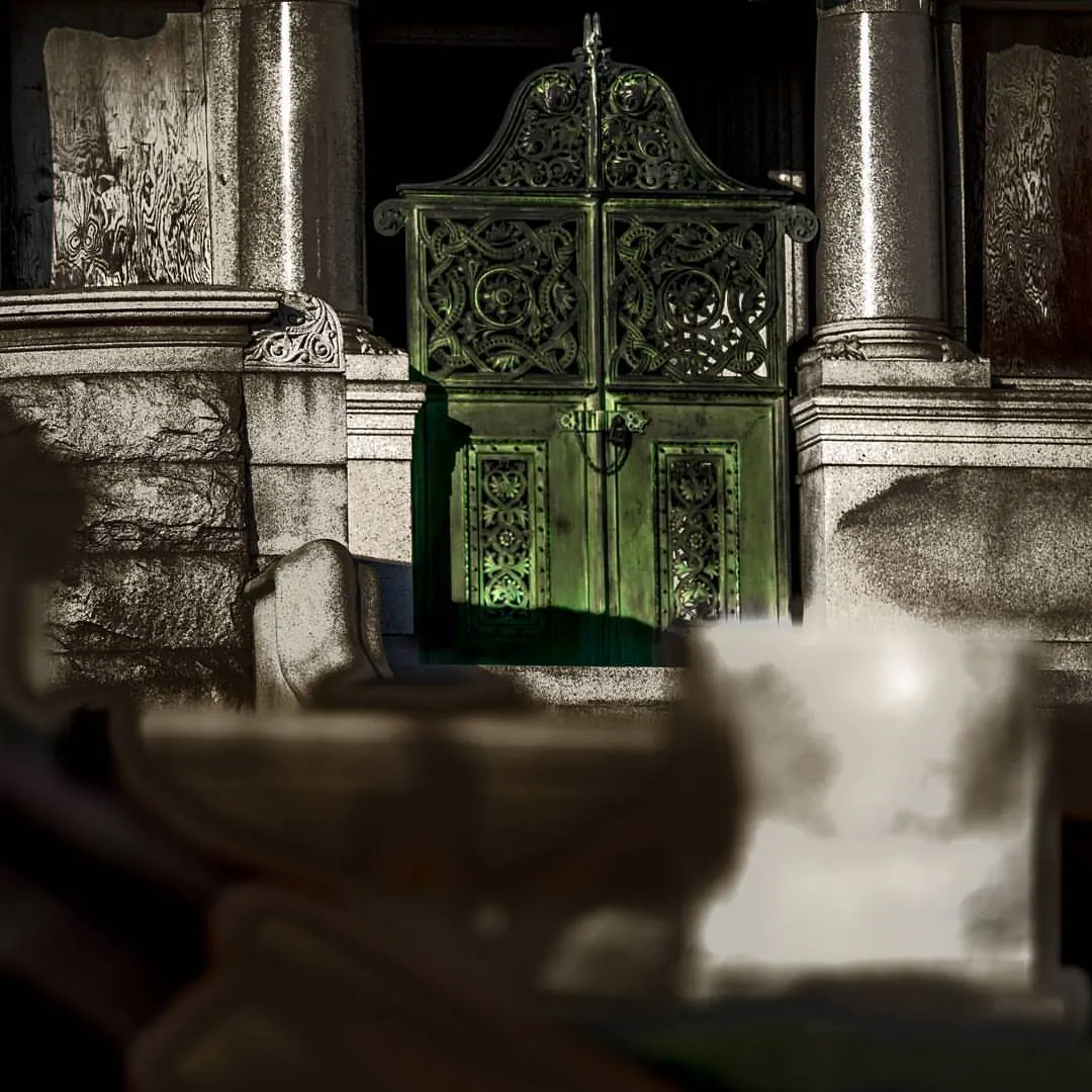 A decorative green metal gate stands within a pale stone entrance.