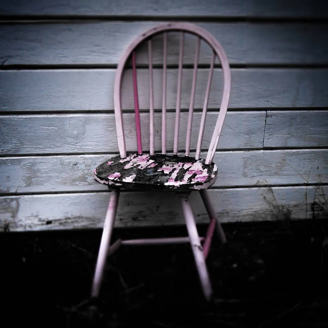 A pale pink chair rests against a softly lit wooden wall.