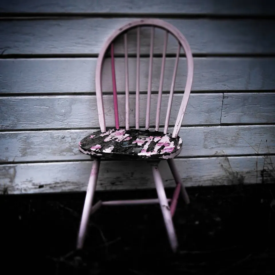 A pale pink chair rests against a softly lit wooden wall.