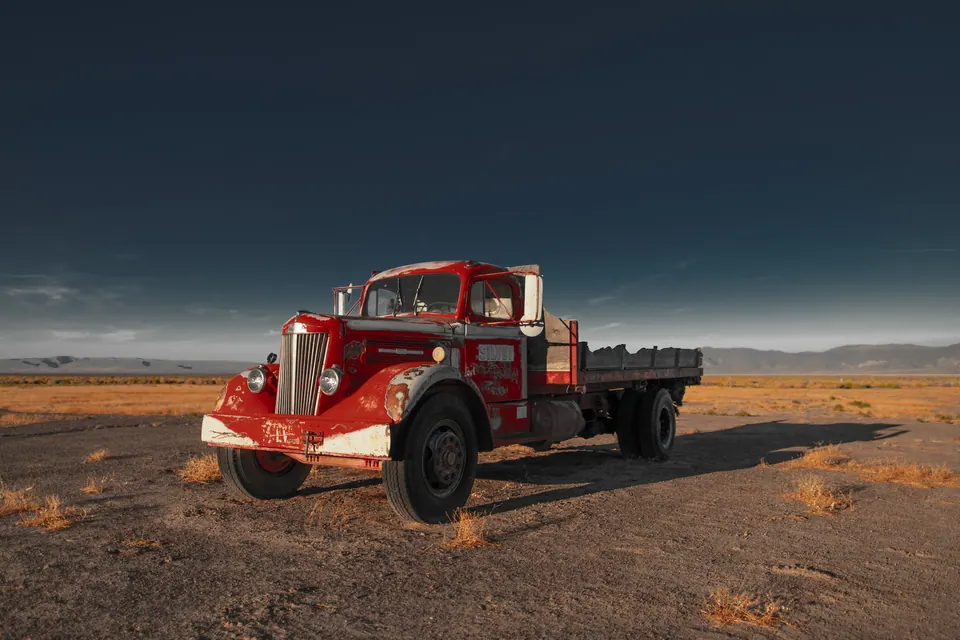 An old red flatbed truck sits alone on an open desert plain.